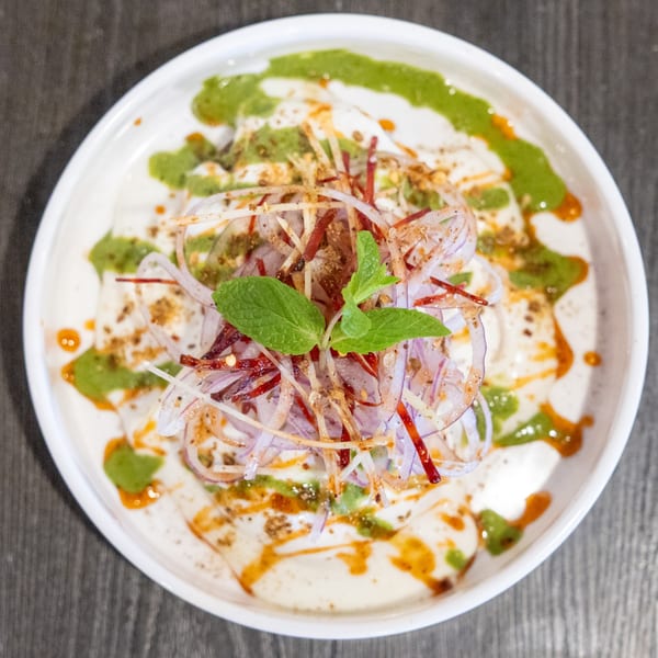 Indian Dahi Bhalla, a yogurt-based dish, topped with green chutney, red onions, and spices.