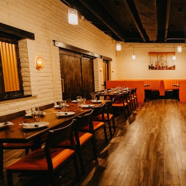 Interior of Tap N Tikka, an Indian restaurant, with long wooden tables, orange chairs, and booth seating.