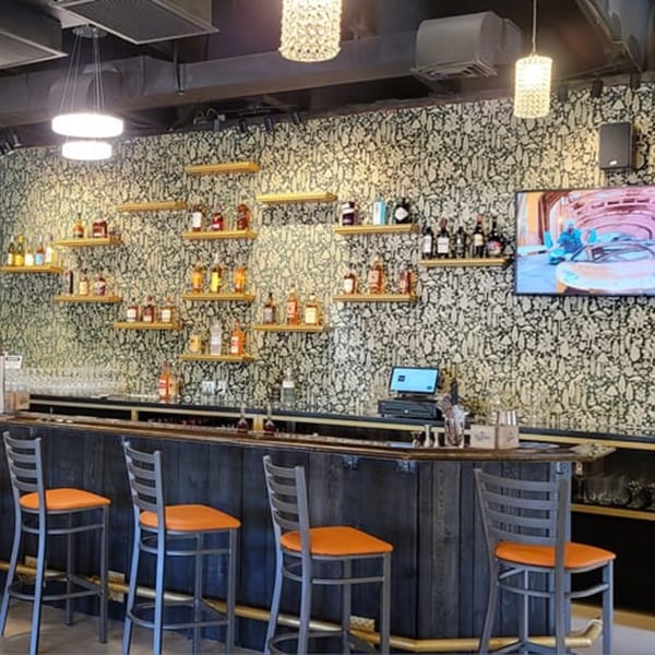 Interior of Tap N Tikka bar with bottles on shelves, orange-seated stools, and a TV.