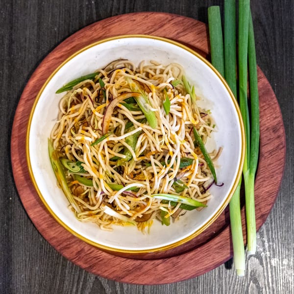 Indian noodles with vegetables and spices in a white bowl, garnished with green onions.