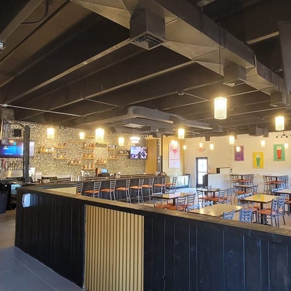 Interior of Tap N Tikka, showing a bar with stools, dining tables, and exposed ceiling ducts.