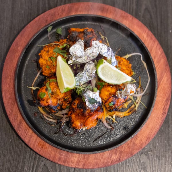 Sizzling Indian chicken tikka with lime wedges and foil-wrapped garlic on a cast iron platter.