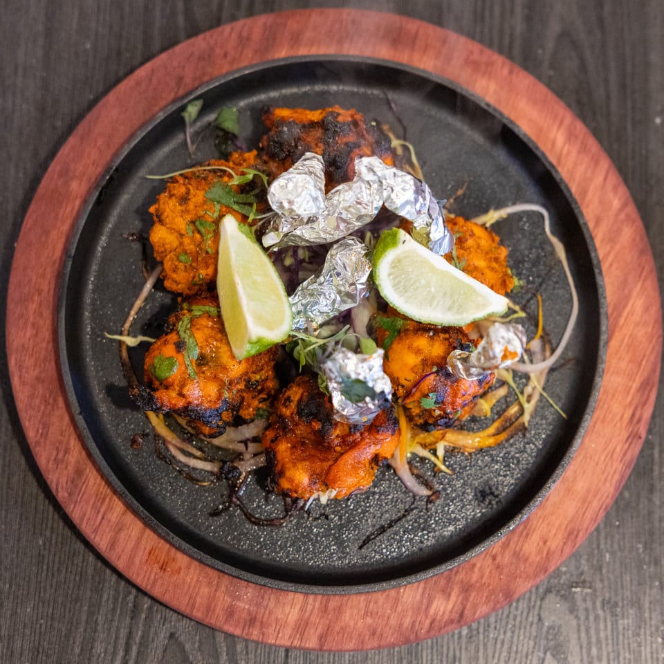 Sizzling Indian chicken tikka with lime wedges and foil-wrapped garlic on a cast iron platter.