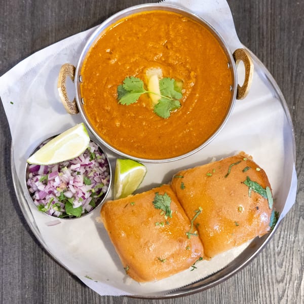 Tap N Tikka's Pav Bhaji, a vibrant Indian vegetable curry with butter, cilantro, chopped onions, and lime.