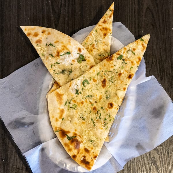 Four pieces of garlic naan bread, garnished with cilantro, served in a white paper-lined basket.