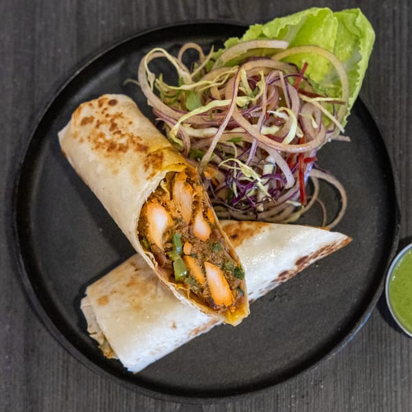 Two Indian chicken tikka wraps with a side of red onion salad and green chutney.