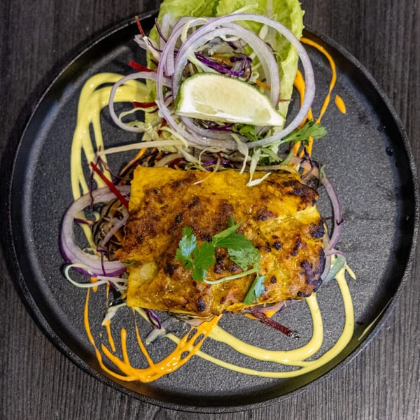 Indian paneer tikka with salad, red onions, lime, and yellow sauces on a black plate.