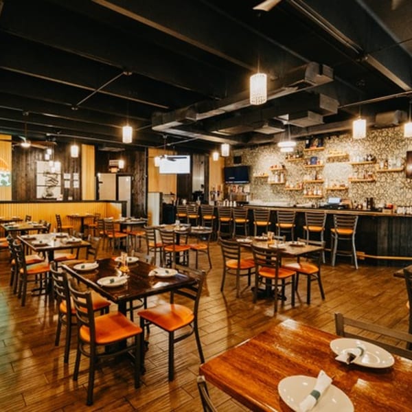 Spacious Tap N Tikka dining room with wooden tables, orange chairs, and a well-stocked bar.