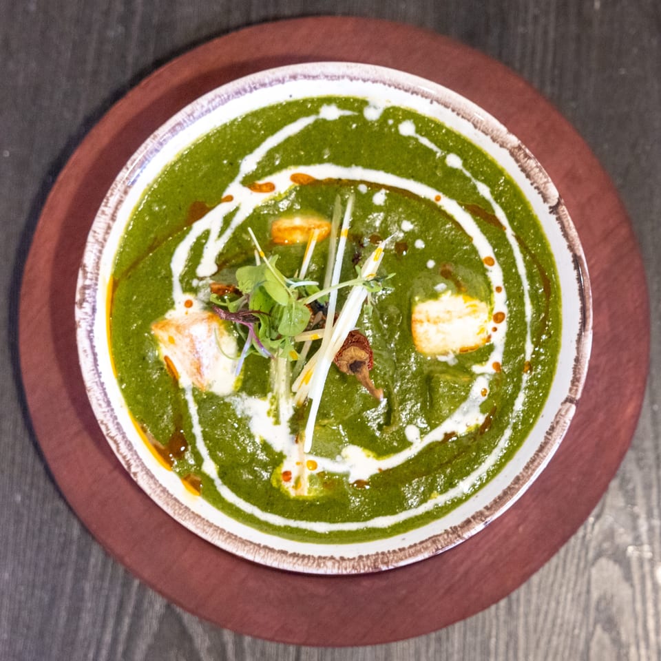 Overhead view of Tap N Tikka's Palak Paneer, a vibrant green Indian dish with paneer and cream swirls.