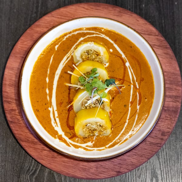 Indian dish with stuffed yellow rolls in a rich orange sauce, garnished with fresh herbs.
