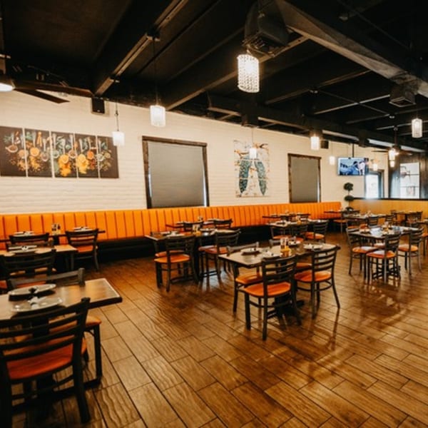 Spacious Tap N Tikka dining room with orange booth seating, dark tables, and wood-look flooring.